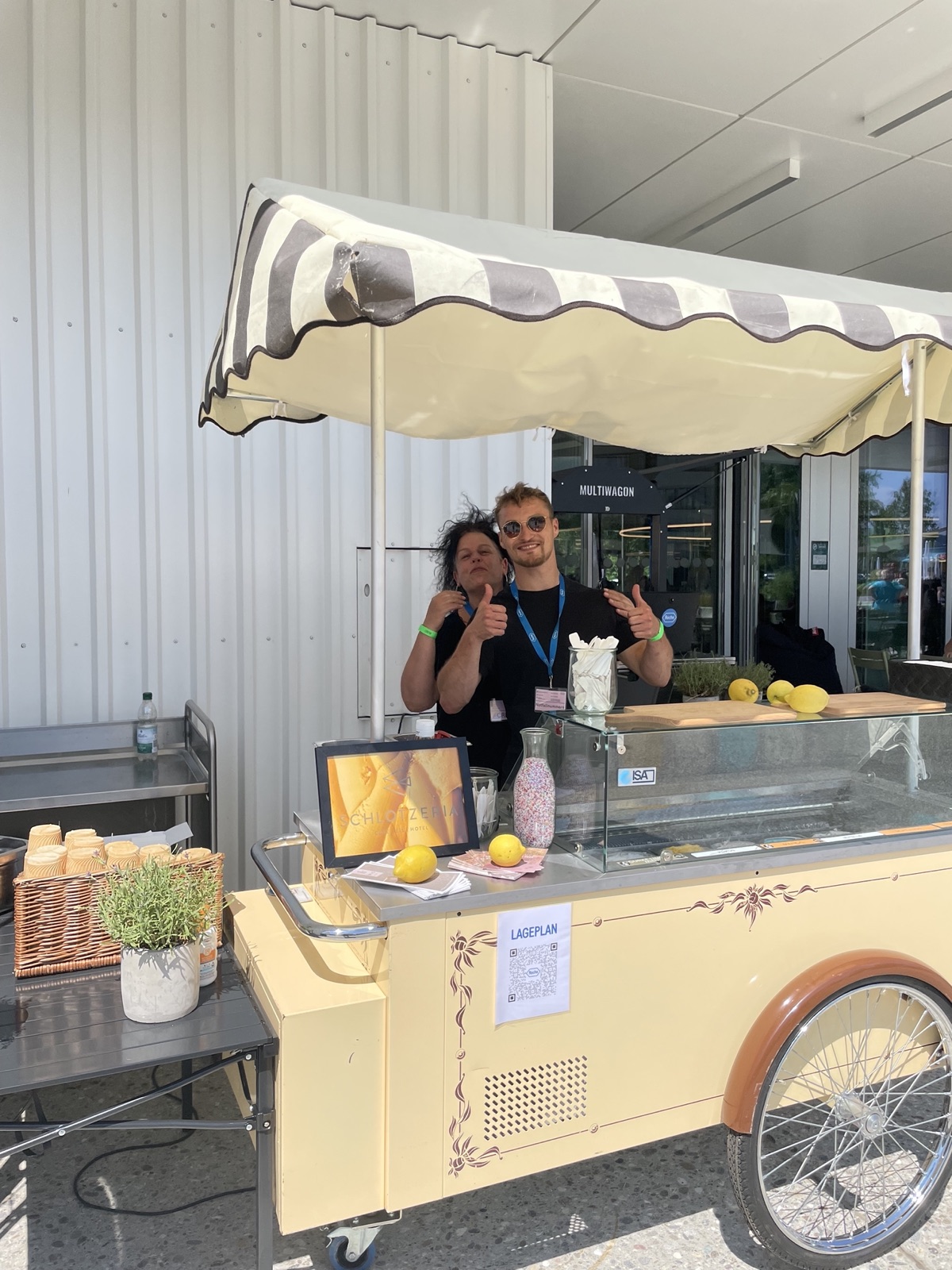 Schlotzeria-Eiswagen mit zwei Mitarbeitern vor Ort — klassischer Eiswagen mit gestreiftem Sonnenschirm