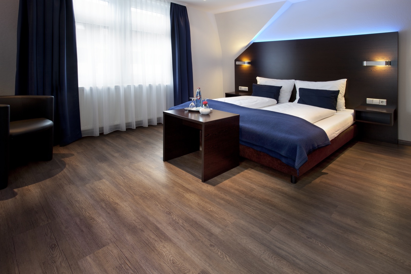 Superior-Doppelzimmer im Hotel Schlotzeria — Doppelbett mit dunkelblauen Kissen und Tagesdecke, dunkler Holzboden